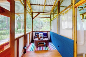 A wooden room with a sloped ceiling, a small round table with a cushion, and a view of greenery outside. - Oceanfront Open-Air Bungalow on Ballena Beach (Uvita)