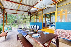 A covered outdoor dining area with a table set for two, chairs, and a view of the surrounding greenery. - Oceanfront Open-Air Bungalow on Ballena Beach (Uvita)