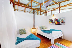 A room with two beds, a wooden ceiling, a colorful artwork on the wall, and a striped rug on the floor. - Oceanfront Open-Air Bungalow on Ballena Beach (Uvita)