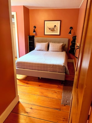A bedroom with a bed, a framed picture on the wall, and a wooden floor.