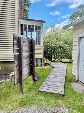 A wooden deck leading to a house with a brick chimney, a small porch with a planter, and a clear sky.