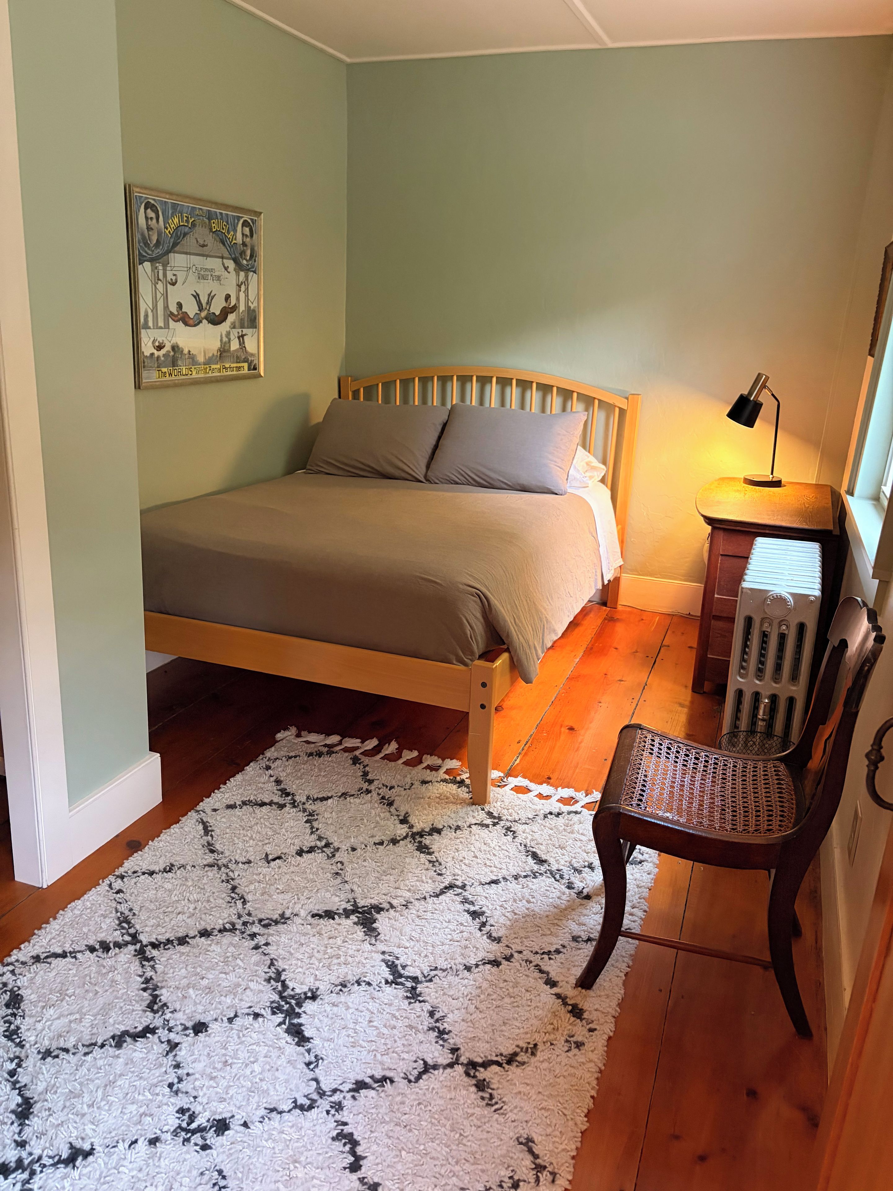 A bedroom with a bed, a chair, a radiator, a lamp, and a poster on the wall.
