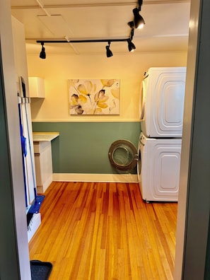 A laundry room with a washing machine, a drying rack, and a painting on the wall.