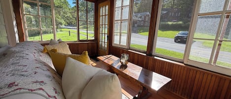 A room with a large bed, a wooden bench, and a view of a street and greenery.