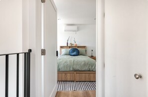 A bedroom with a bed, bedside table, lamp, and a wall-mounted air conditioner. - Stylish 3BR Windsor Hills Retreat Near SoFi & LAX (View Park-Windsor Hills)