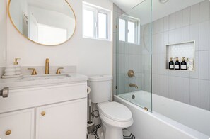 A modern bathroom with a white vanity, gold fixtures, a glass-enclosed shower, and a toilet with a water-saving label. - Stylish 3BR Windsor Hills Retreat Near SoFi & LAX (View Park-Windsor Hills)