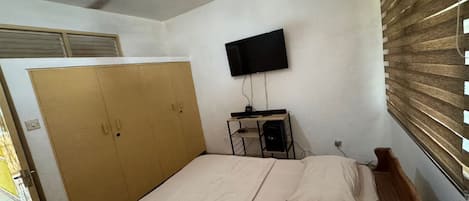 A bedroom with a bed, a wardrobe, a television, and a ceiling fan.