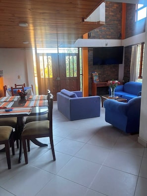 A dining area with a table and chairs, a blue sofa, and a television mounted on a brick wall.