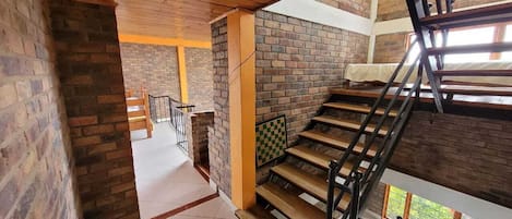 Una escalera de madera con barandales de metal que conduce a un piso superior con vistas a zonas verdes.