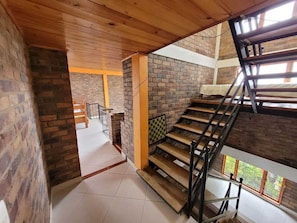 A staircase with wooden steps and metal railings, leading to an upper floor with a view of greenery outside.