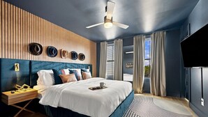 Quarto de hotel moderno com uma cama grande, ventilador de teto e televisão na parede.