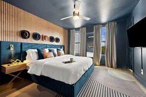 Moderni hotellihuone, jossa on suuri sänky, kattotuuletin ja seinälle asennettu televisio.
