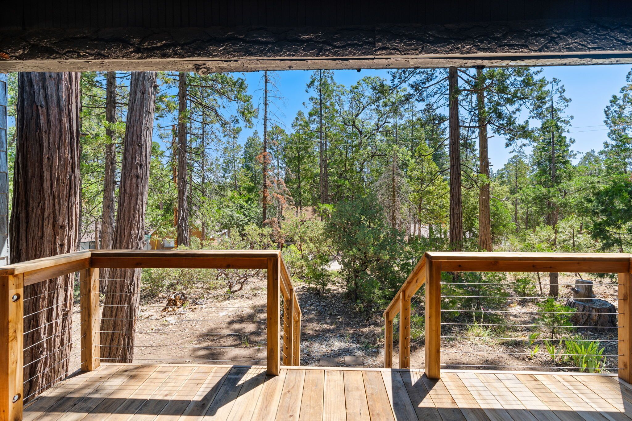 A wooden deck with a metal railing overlooking a forested area.