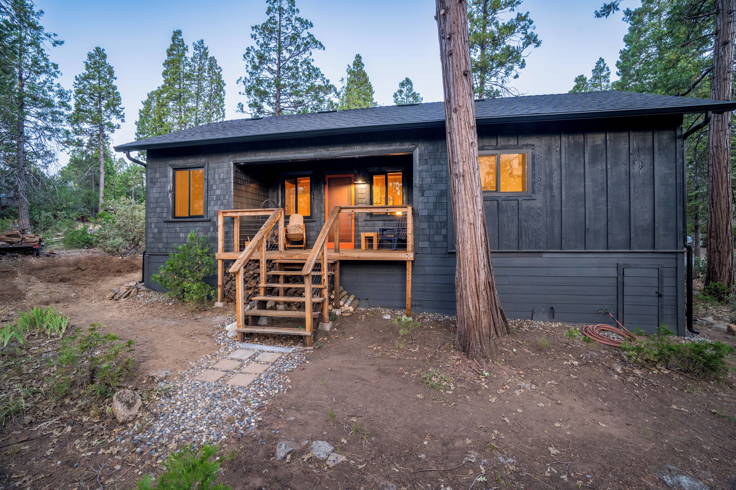 A cabin with a wooden deck, a staircase, and a window with a view of the surrounding forest.