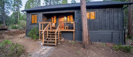 A cabin with a wooden deck, a staircase, and a window with a view of the surrounding forest.