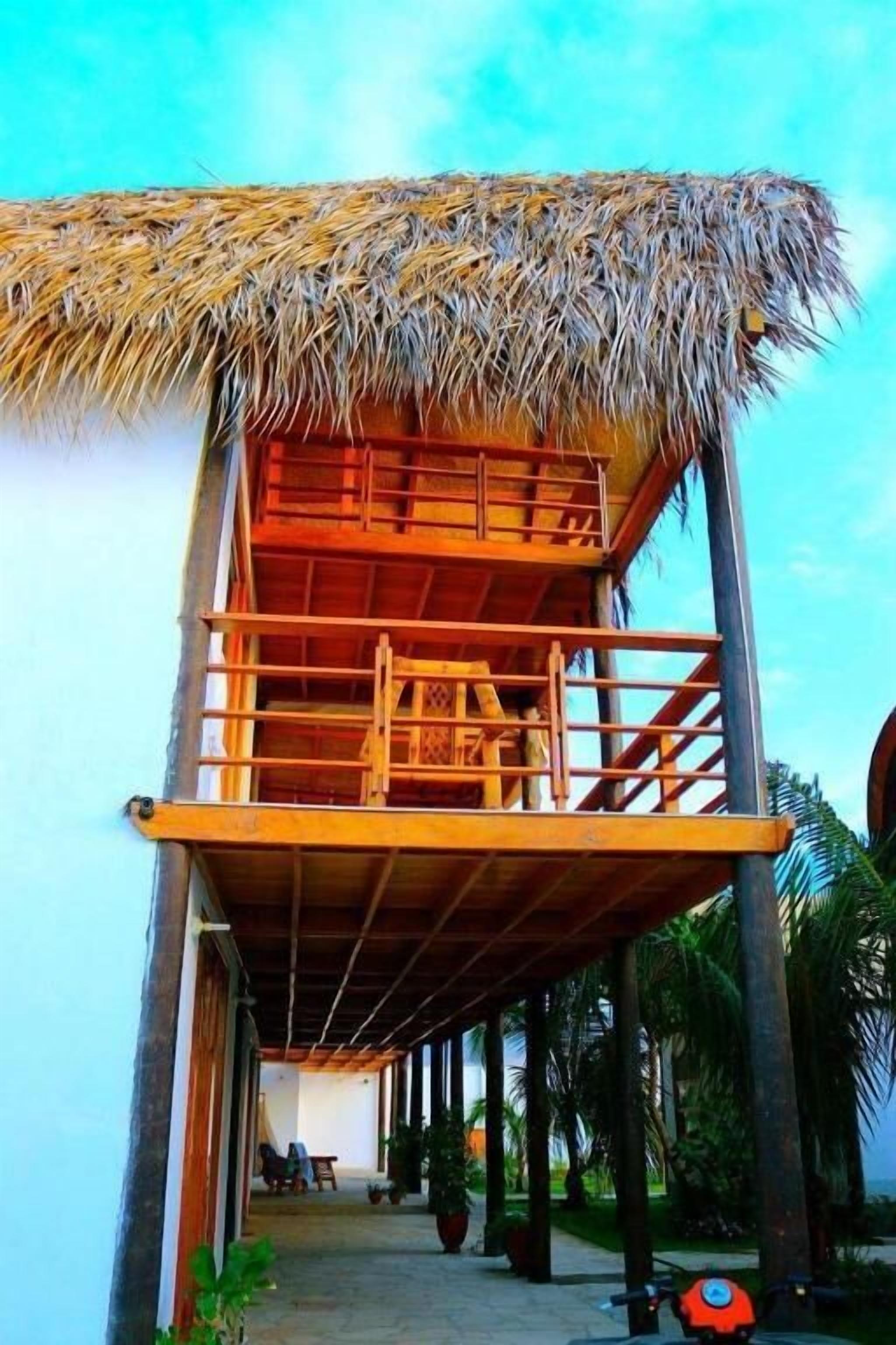 Una estructura de techo de paja con un balcón de madera, rodeada de palmeras.