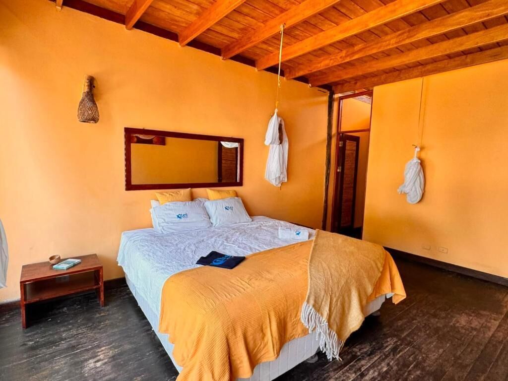 Een slaapkamer met een bed, nachtkastje, handdoek, spiegel en houten plafond.