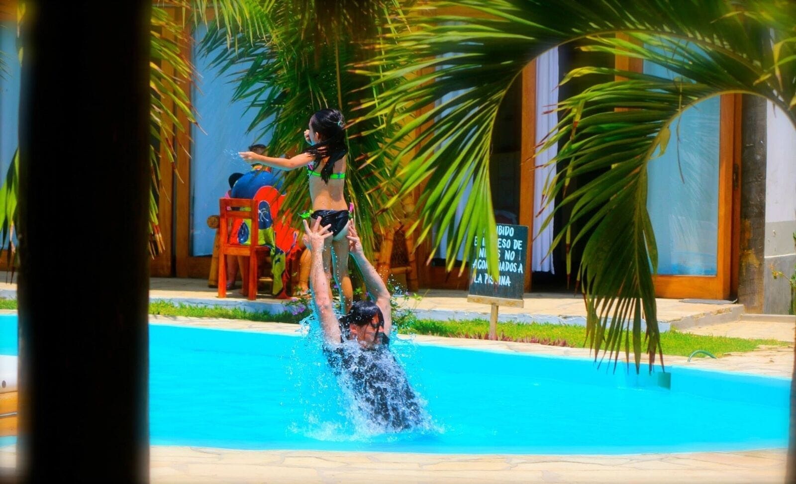 Una piscina con alguien nadando y otra persona en el borde.