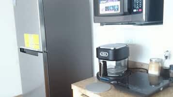 Een keuken met een koelkast, magnetron, koffiezetapparaat en een klein aanrecht.