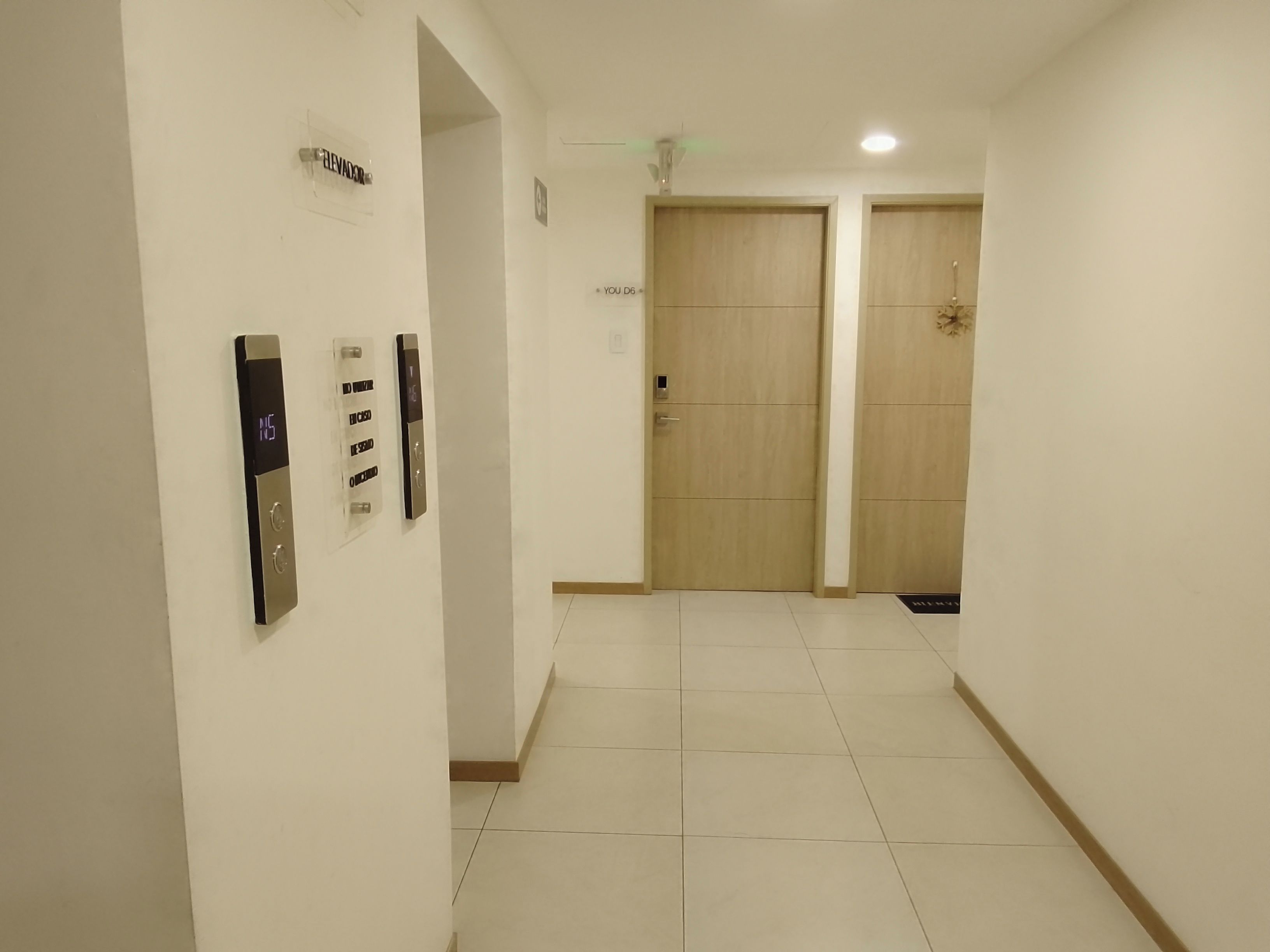 A hallway with two wooden doors, an elevator, and a sign indicating the direction to the elevator.