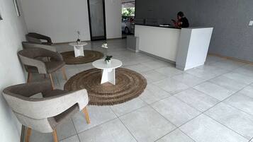 Zona de recepción con recepcionista, mostrador y área de estar con sillas y mesas.