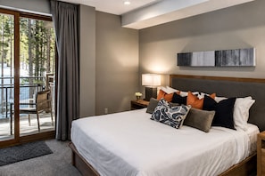A hotel room with a large bed, a nightstand with a lamp, a view of trees through a window, and a balcony with a chair. - 1-Bedroom Ski in Ski Out Hotel Peak 8 Breckenridge 2/13/27 - 2/20/27 (Breckenridge)