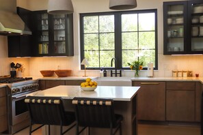 Una cocina moderna con una isla central, muebles oscuros y un amplio ventanal que proporciona luz natural.