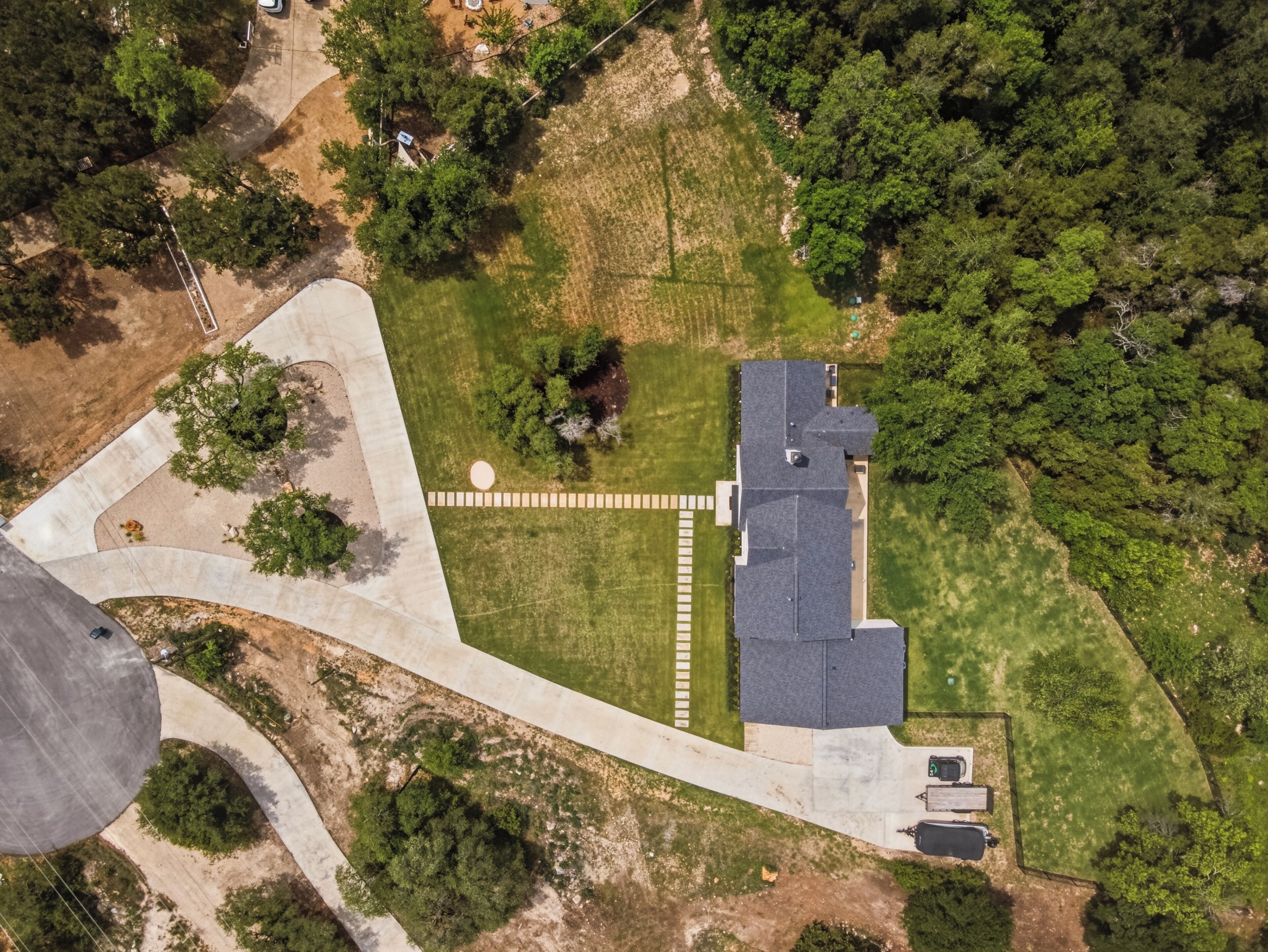 Vista aérea de um bairro residencial com uma casa, entrada de automóveis pavimentada e vegetação ao redor.