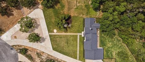 An aerial view of a residential area with a house, a paved driveway, and surrounding greenery.