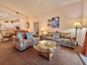 A living room with two patterned sofas, a glass coffee table, and a dining area with wicker furniture. - 3BR Orlando Area Condo | Resort Pools & Pickleball (Davenport)