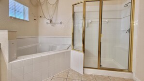 A bathroom with a bathtub, a glass-enclosed shower, and a window with blinds. - 3BR Orlando Area Condo | Resort Pools & Pickleball (Davenport)