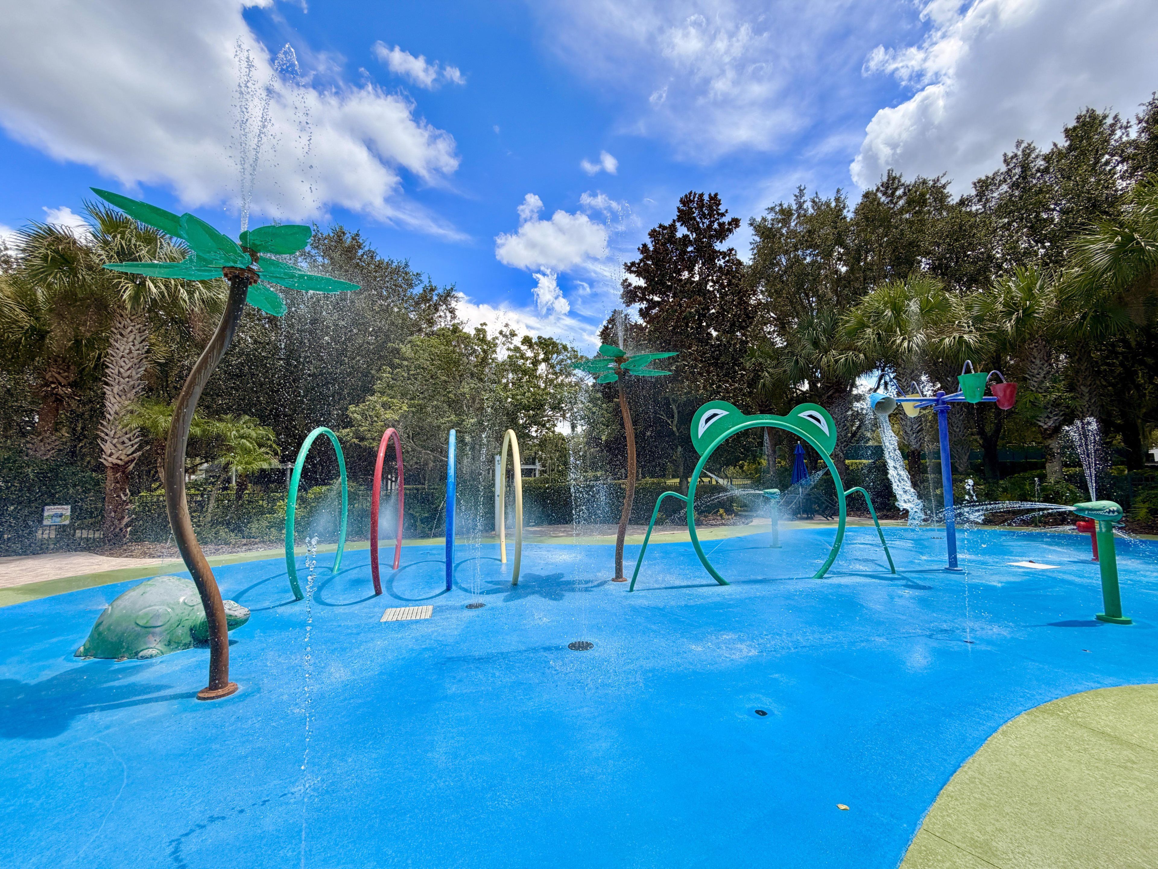 Un área de juegos acuáticos al aire libre con múltiples fuentes de colores y una estructura con forma de rana.