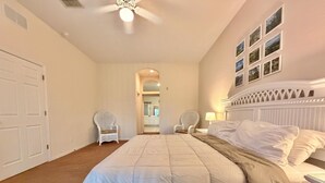 A bedroom with a bed, two chairs, a nightstand, a ceiling fan, and a hallway leading to another room. - 3BR Orlando Area Condo | Resort Pools & Pickleball (Davenport)
