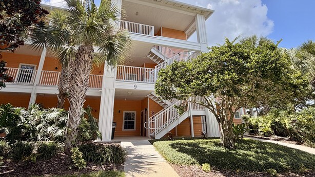 A multi-story building with a central staircase, surrounded by greenery and palm trees. - 3BR Orlando Area Condo | Resort Pools & Pickleball (Davenport)
