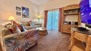A living room with a sofa, a coffee table, a TV, and a wicker side table. - 3BR Orlando Area Condo | Resort Pools & Pickleball (Davenport)