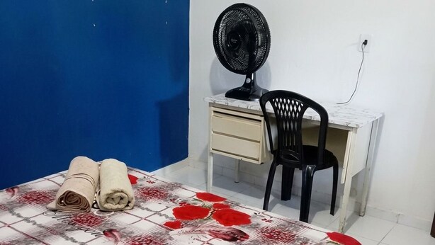 A room with a bed, a desk, a chair, and a standing fan.