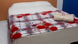 A bed with a floral-patterned bedspread, a rolled towel, and a wooden headboard.