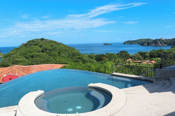 A swimming pool with a view of the sea and a hill.