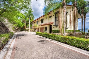 A two-story building with a paved driveway, surrounded by greenery and a clear sky. - Ocean-View Retreat! Playa Penca Resort Condo (Playa Penca)