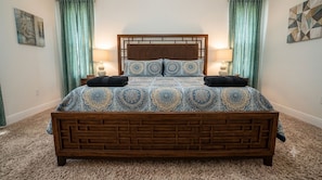A bed with a patterned bedspread and two pillows, flanked by two bedside lamps, in a room with a carpeted floor and curtains.