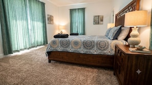 A bedroom with a large bed, a wooden headboard, a nightstand with a lamp, and a carpeted floor.