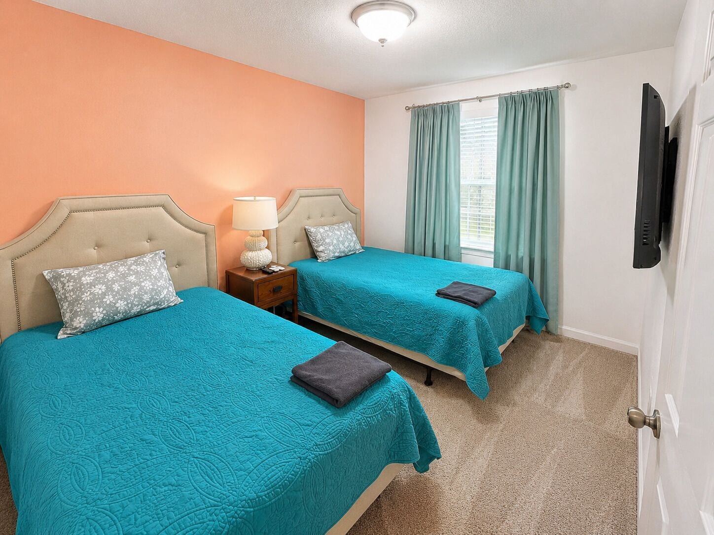 A hotel room with two beds, a nightstand, a lamp, a television, and a window with curtains.