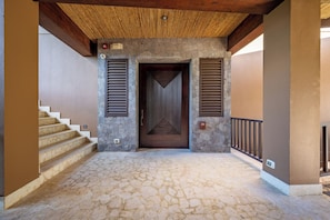 Un acceso cubierto con un muro de piedra, una puerta de madera y una escalera que sube a un nivel superior.