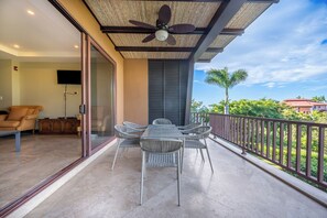 Een balkon met een tafel en stoelen, een plafondventilator en uitzicht op de omgeving.