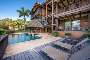 Un área de piscina con sillones de descanso y una estructura de techo de paja.