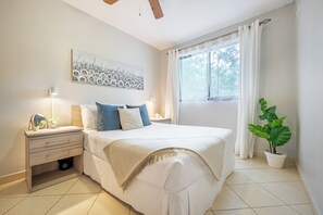 Een slaapkamer met een bed, nachtkastjes, een kunstwerk aan de muur, een raam met gordijnen en een kamerplant.