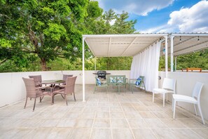 Een terras buiten met een overdekte zithoek, een tafel en stoelen.