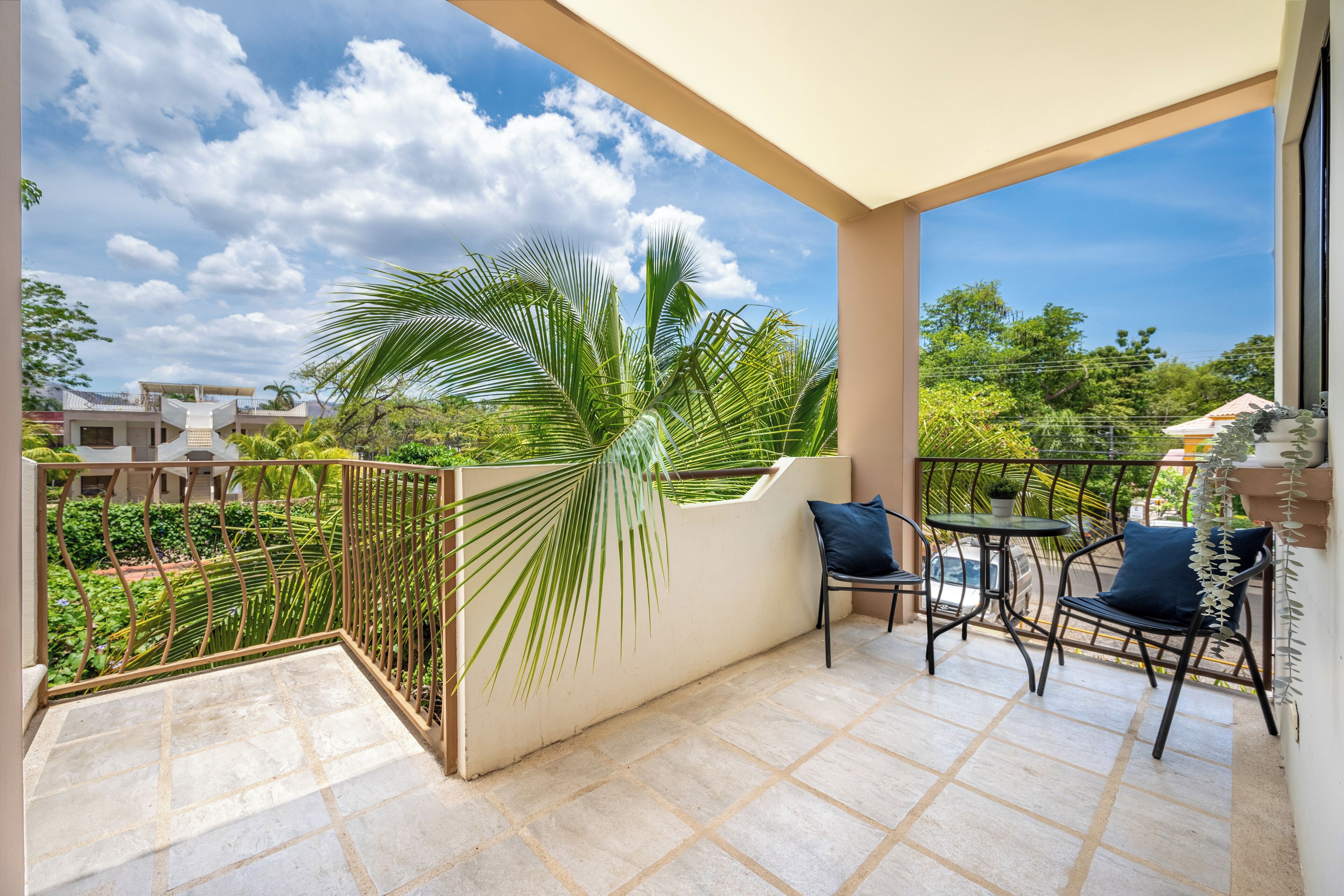 Un balcon doté d’un sol carrelé, d’une rambarde en métal et offrant une vue sur un quartier résidentiel avec des maisons et de la verdure.