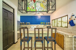 A kitchen with a blue wall, a stove, a sink, and a bar area with stools. - Playa Carrillo: Private Pool, 1 Mi to Beach (Playa Carrillo)