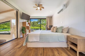 A bedroom with a bed, a TV, a ceiling fan, and a view of greenery outside. - Stylish 'Casa Nonos' Home w/ Yard & Fire Pit! (Playas del Coco)